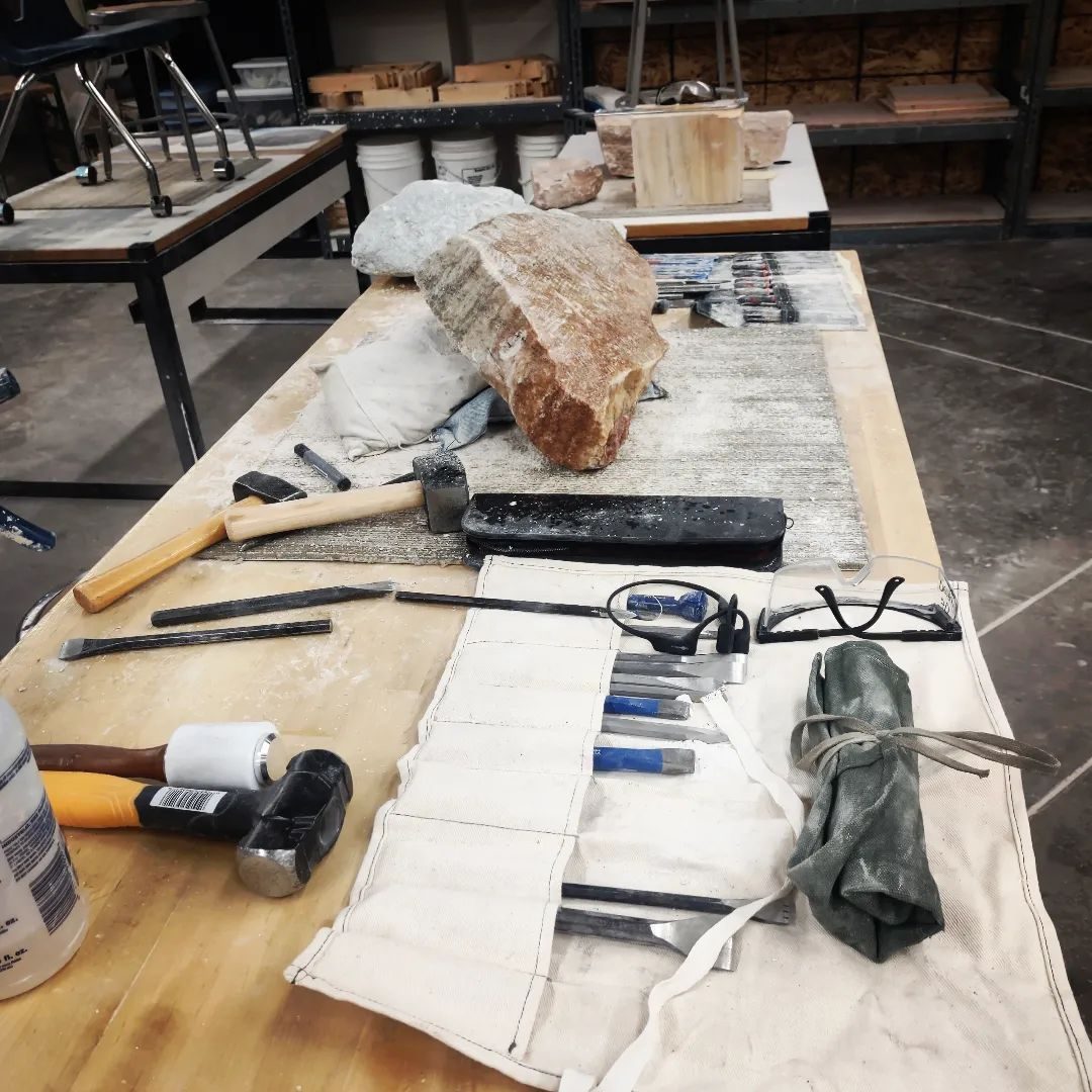 A carving bench laid out with hammers, chisels and a block of stone